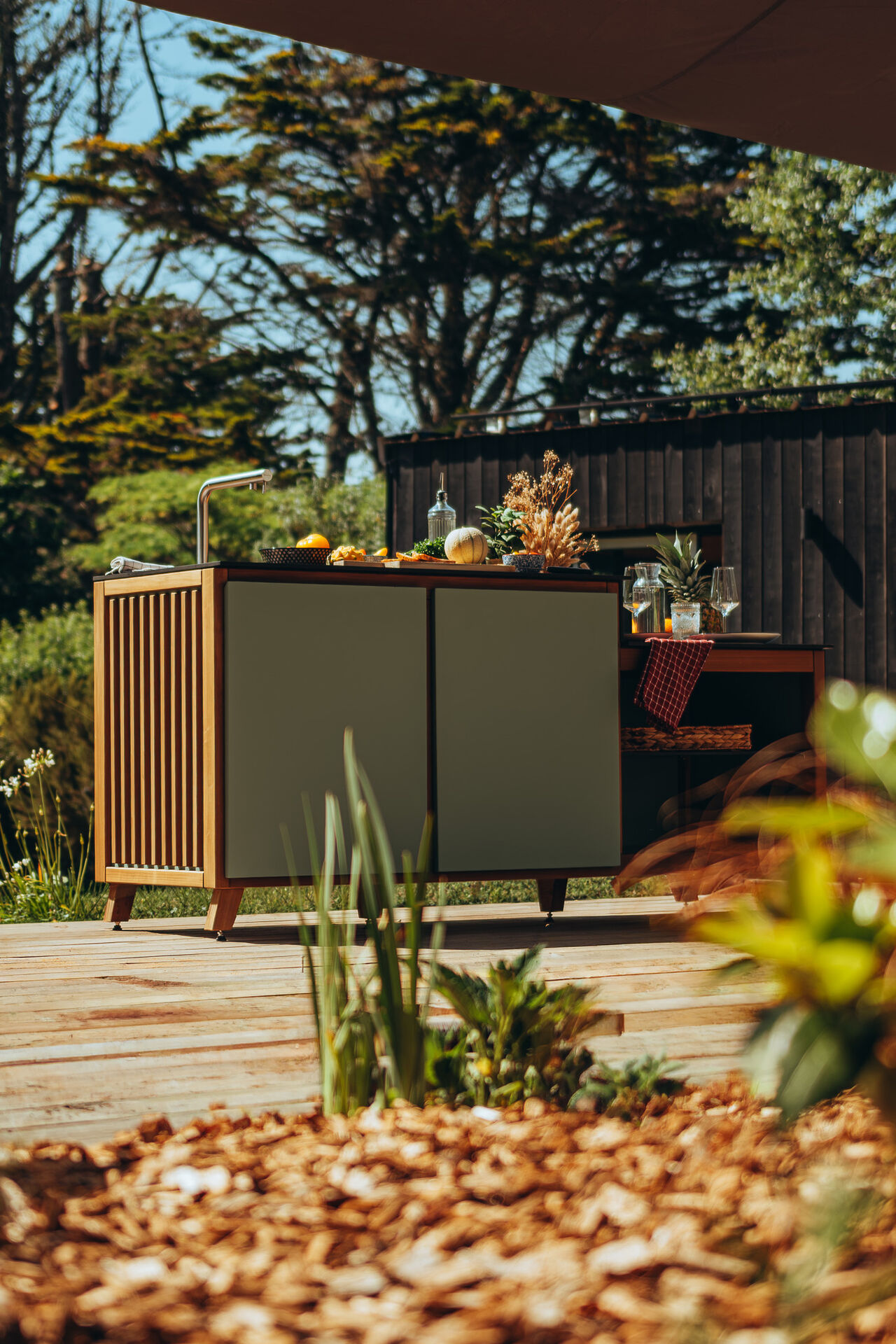Cuisine d'extérieur moderne sur une terrasse en bois ensoleillée.