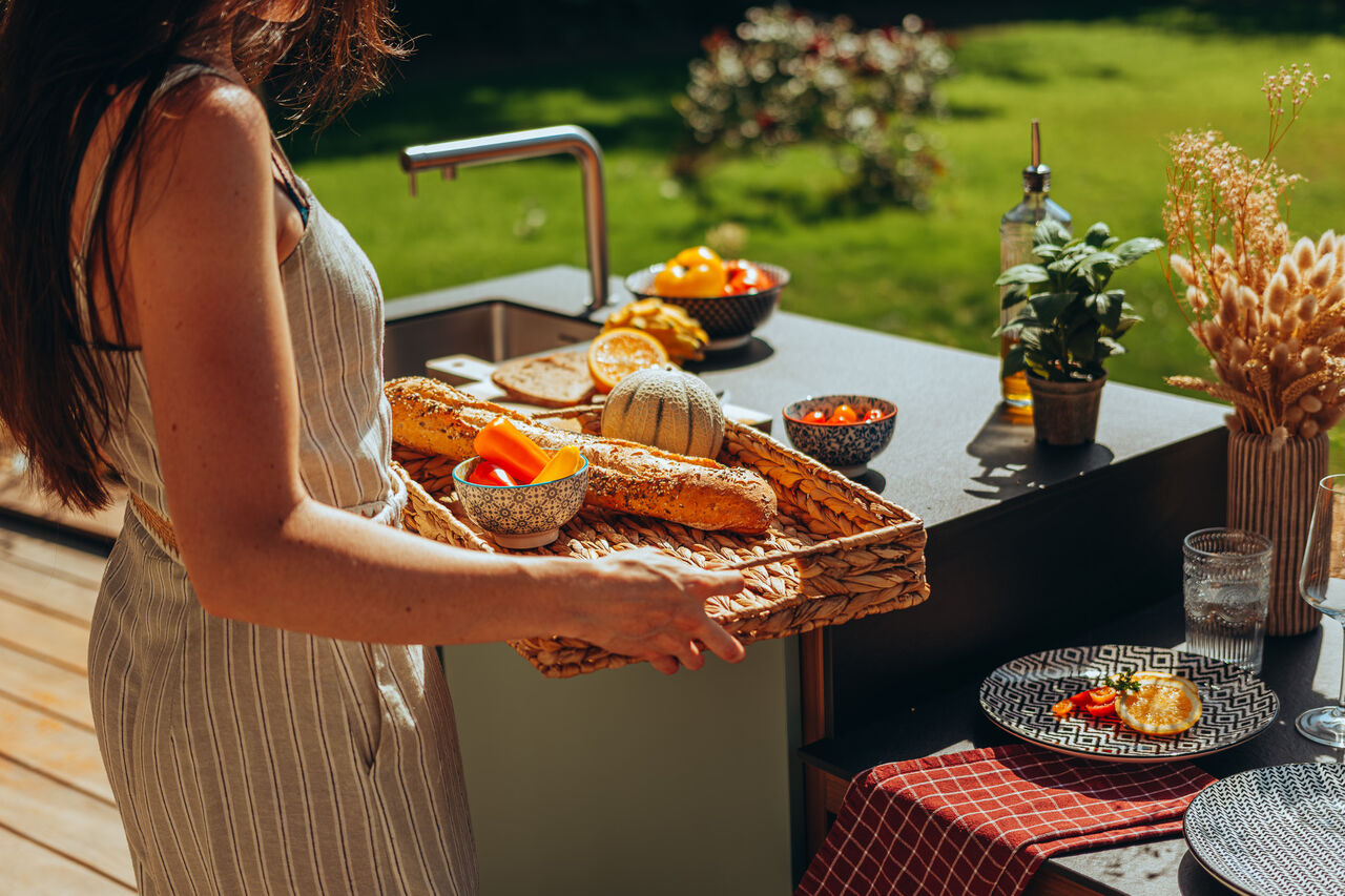 Femme tenant un plateau de nourriture dans une cuisine extérieure.