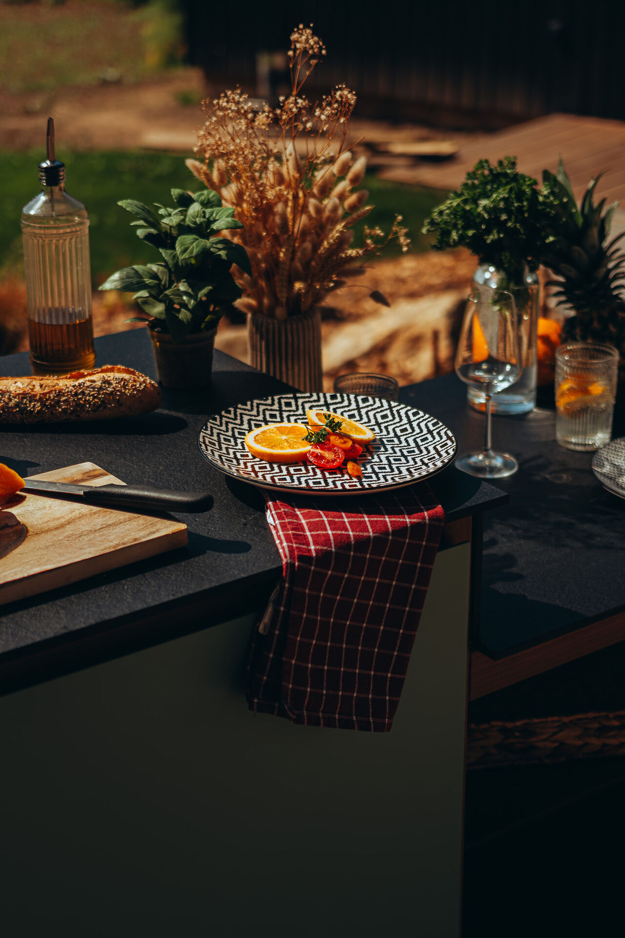 Table de jardin ensoleillée avec fruits, pain et plantes.