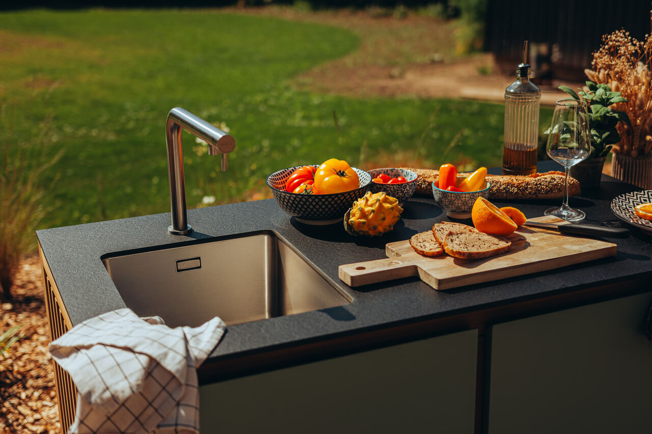 Cuisine d'été avec évier, légumes et pain dans un jardin.